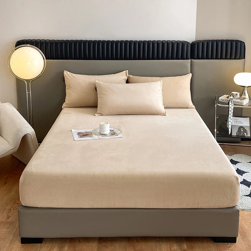A beige luxury velvet bedding set displayed on a bed with dark gray upholstered headboard and bedside lamp.