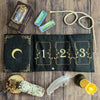 A black velvet pouch with gold detailing holds three tarot cards and a feather on a wooden surface.