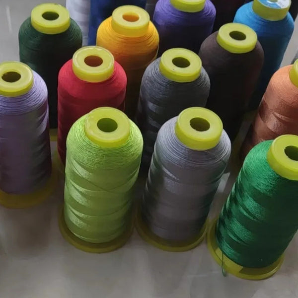 A collection of spools of high tenacity polyester sewing thread in various colors including green, purple, orange, and blue.