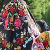 A close-up of a dark fabric featuring colorful floral embroidery done with gradient cross stitch threads.