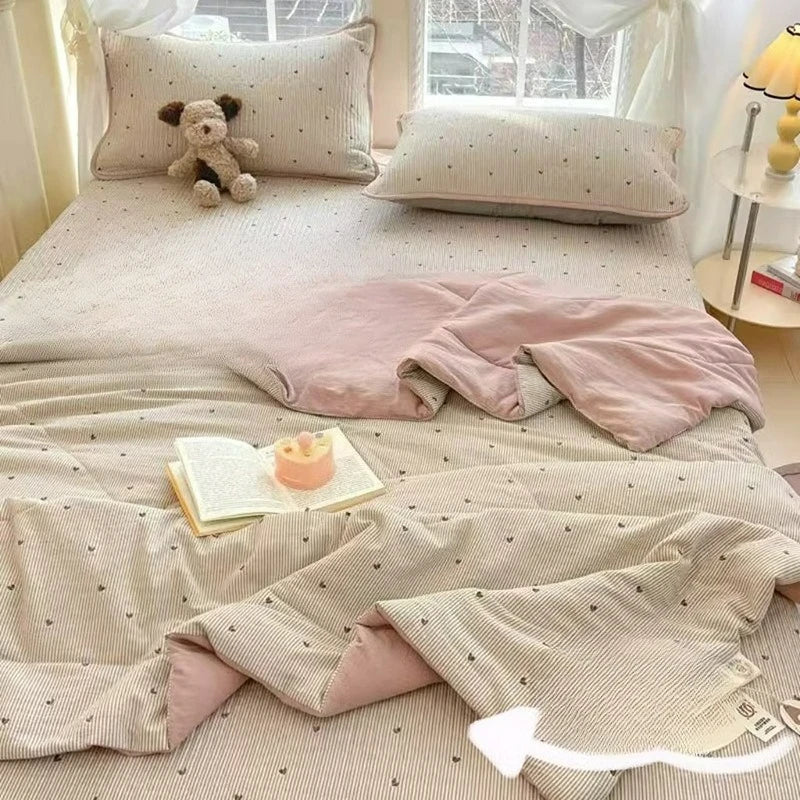 A light beige cartoon quilting comforter with pink accents and matching pillows on a bed.