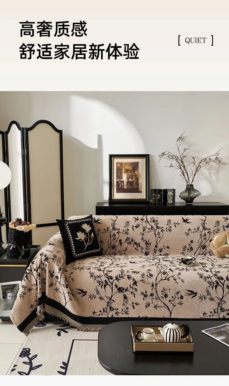 A beige chenille sofa slipcover with black floral patterns displayed in a bright interior setting.