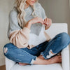 A woman wearing a light gray knitted sweater is sitting down, holding yarn for knitting or crochet.