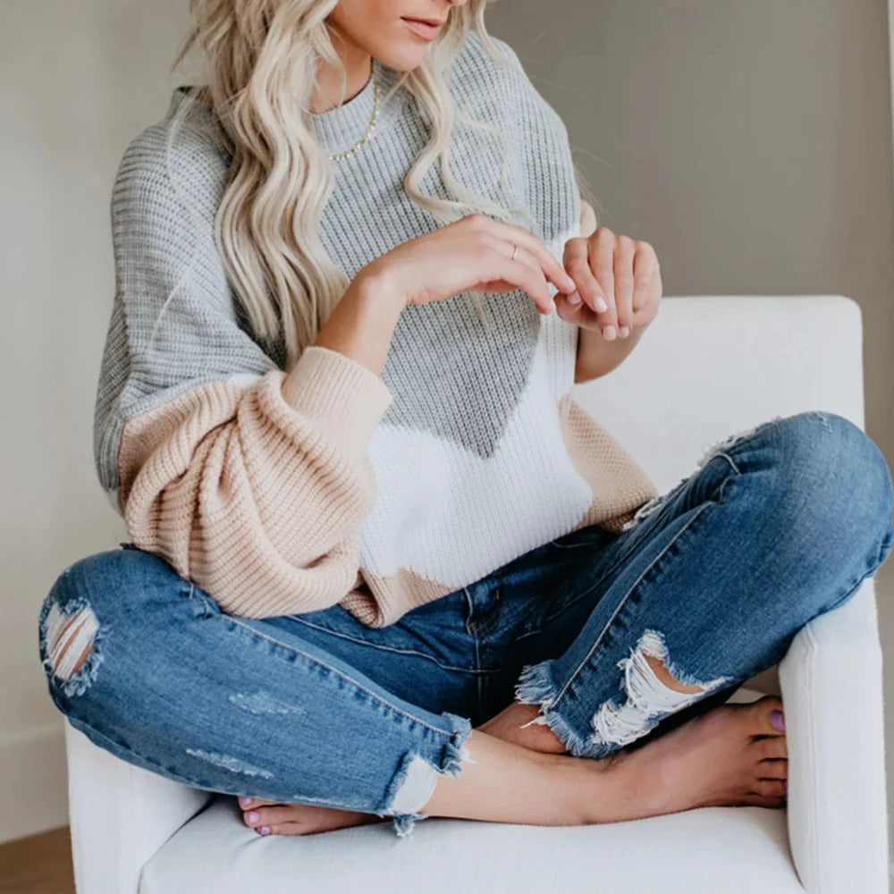 A woman wearing a light gray knitted sweater is sitting down, holding yarn for knitting or crochet.