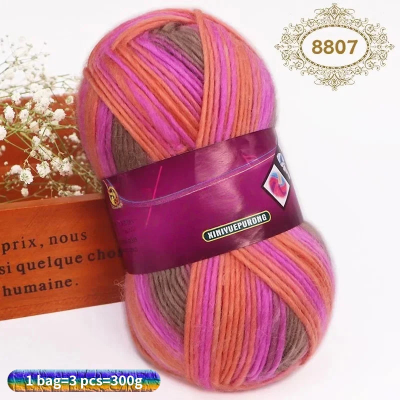 A skein of gradient dyed wool yarn in shades of pink, purple, and orange is displayed next to a wooden box.