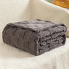 A dark gray checkered fleece throw blanket folded neatly on a cream-colored, fluffy surface.