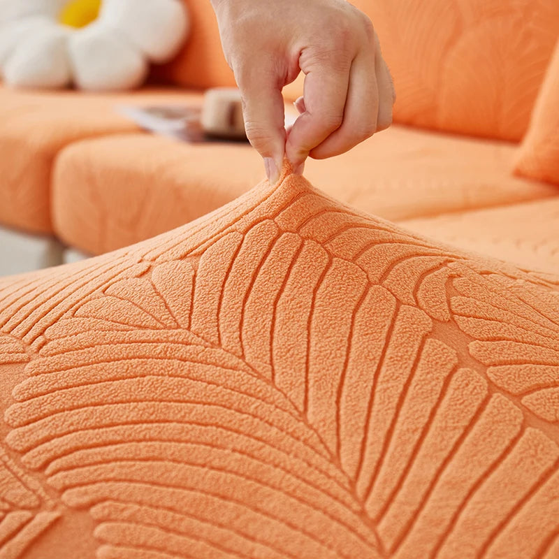 A hand is adjusting the textured orange leaf jacquard stretch sofa cover on an orange sofa.