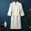 A white cotton terry robe hanging on a wooden hanger against a dark blue wall.