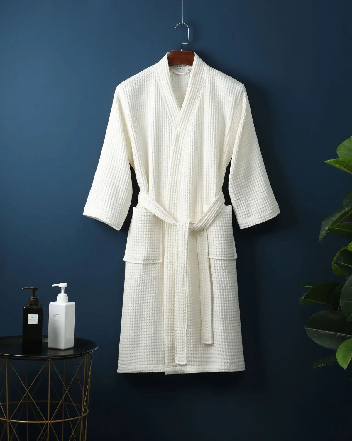 A white cotton terry robe hanging on a wooden hanger against a dark blue wall.