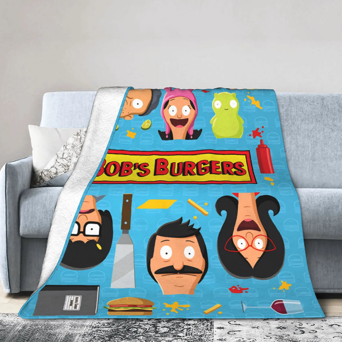 A blue throw blanket featuring cartoon characters from Bob's Burgers, including Tina Belcher and Linda Belcher.