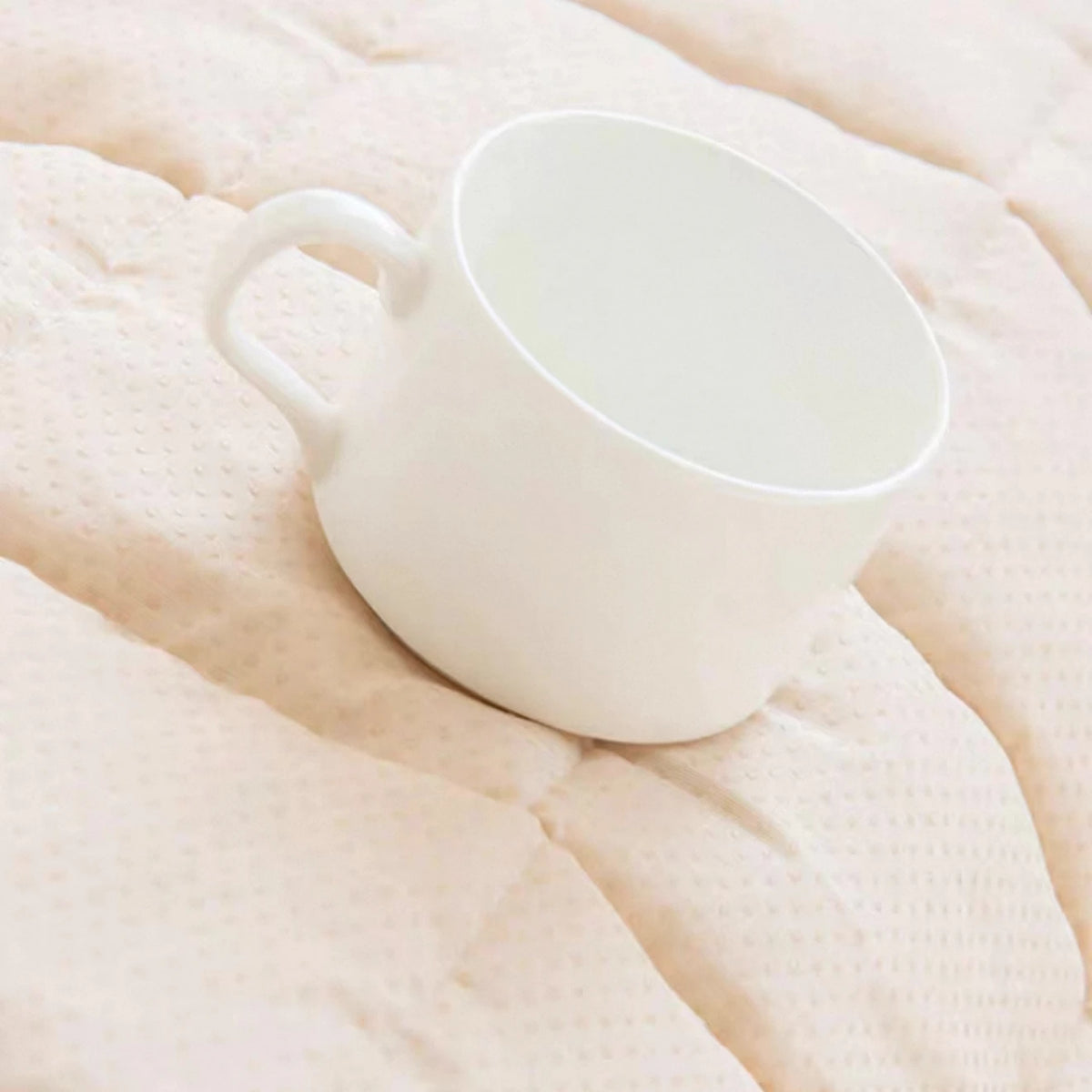A white ceramic pitcher resting on a light pink flannel fabric.
