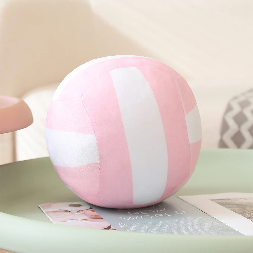 Pink and white striped plush volleyball ball cushion resting on a light green surface.