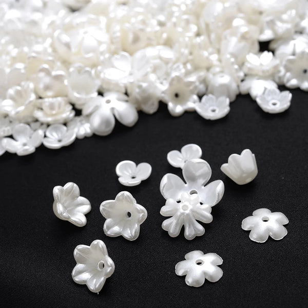 A close-up of small, white imitation pearl flower spacer beads scattered on a dark surface.