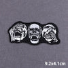 Three black embroidered patches depicting skull faces in white and gray.
