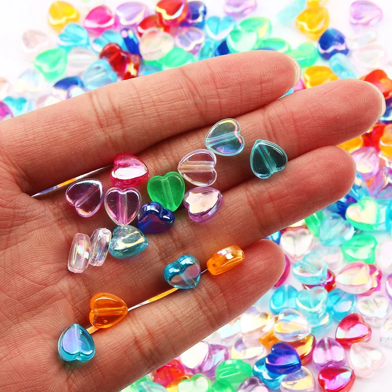 A hand holds a collection of colorful acrylic heart beads for jewelry making.