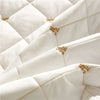 Close-up of white quilted fabric with gold embroidery on a bed skirt.
