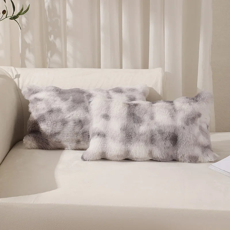 Three gray faux rabbit fur decorative throw pillows resting on a white bed with sheer curtains.