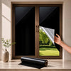 A hand holds a roll of reflective mirror window film next to a dark-framed window.