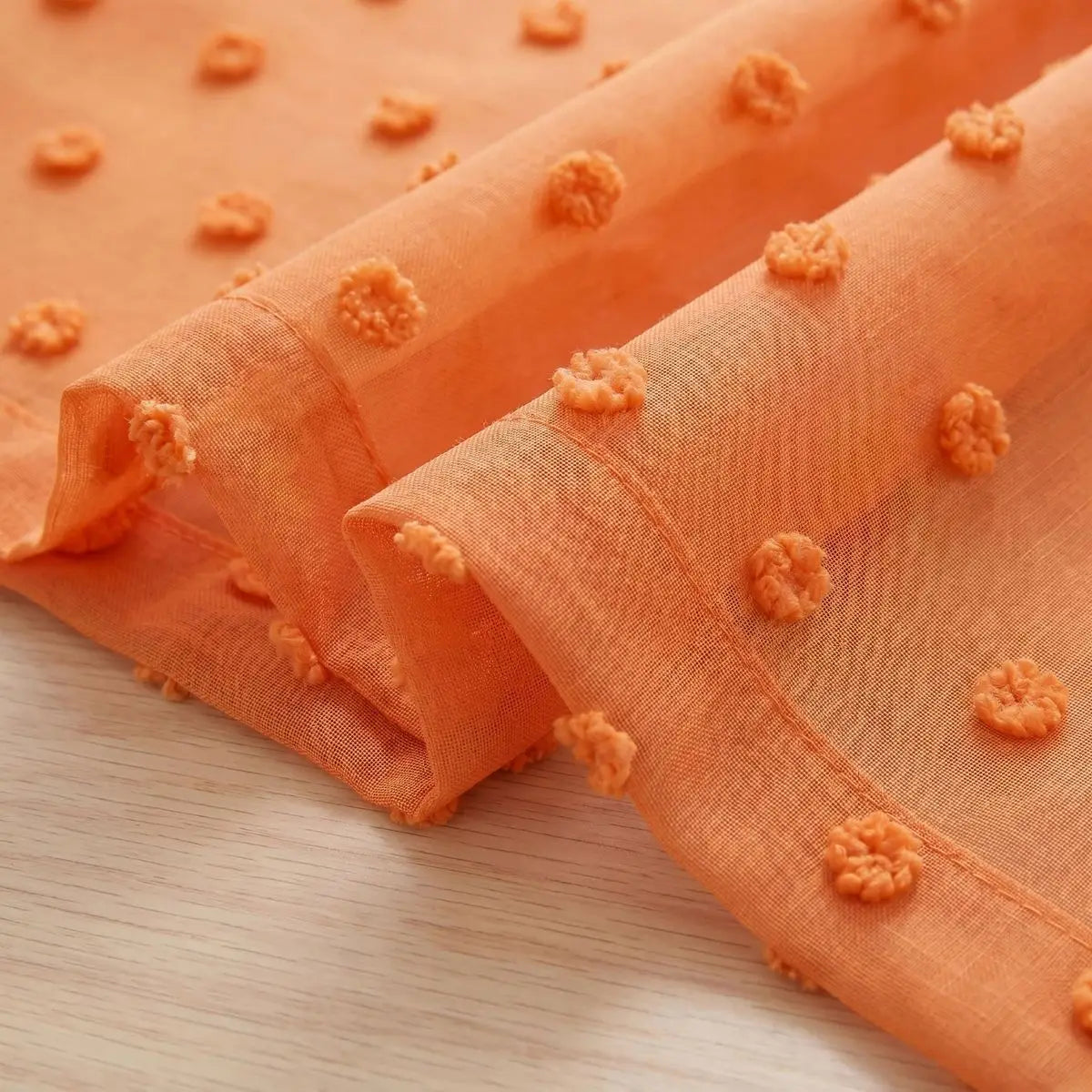 Orange pompoms scattered on a sheer fabric curtain rolled in a soft orange hue.
