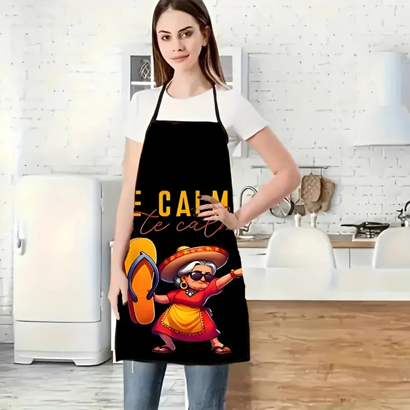 A woman wearing a black apron with a colorful Mexican-inspired character design standing in a kitchen.