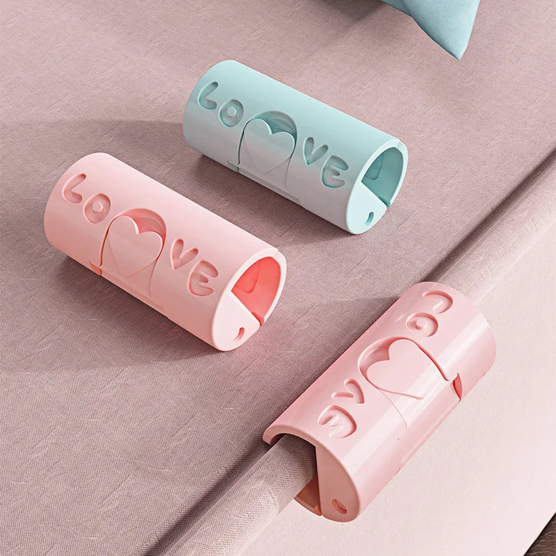 Pink and light blue non-slip bed sheet grippers with heart-shaped clips shown on a pink fabric.