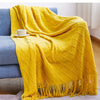 A bright yellow knitted tassel throw blanket draped over a blue sofa.