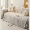 A beige sofa cover featuring an elegant fishbone pattern, decorated with a cream pillow and a white knitted sphere.