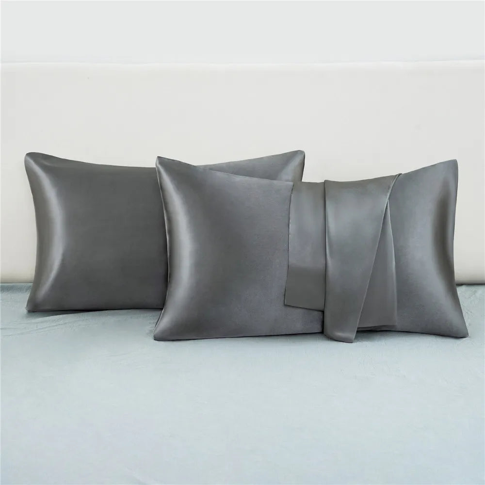 A set of four silky satin pillow covers in a muted gray color displayed on a light blue bed.