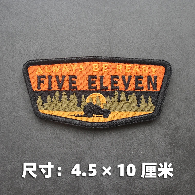 An embroidered patch with the text ALWAYS BE READY FIVE ELEVEN and a silhouette of a vehicle against a forest background.