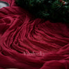 A deep red crinkled cheesecloth table runner draped next to a green wreath with pinecones.