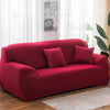 A deep red stretch sofa cover with two accent pillows placed in a bright living room.