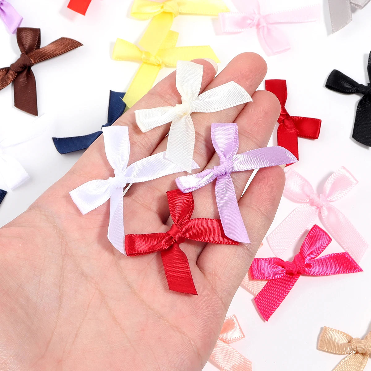 A hand holds various satin ribbon bows in pink, red, purple, white, and yellow colors.