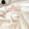 A pink embroidered flower appliqué on a white satin fabric, next to a glass bottle.