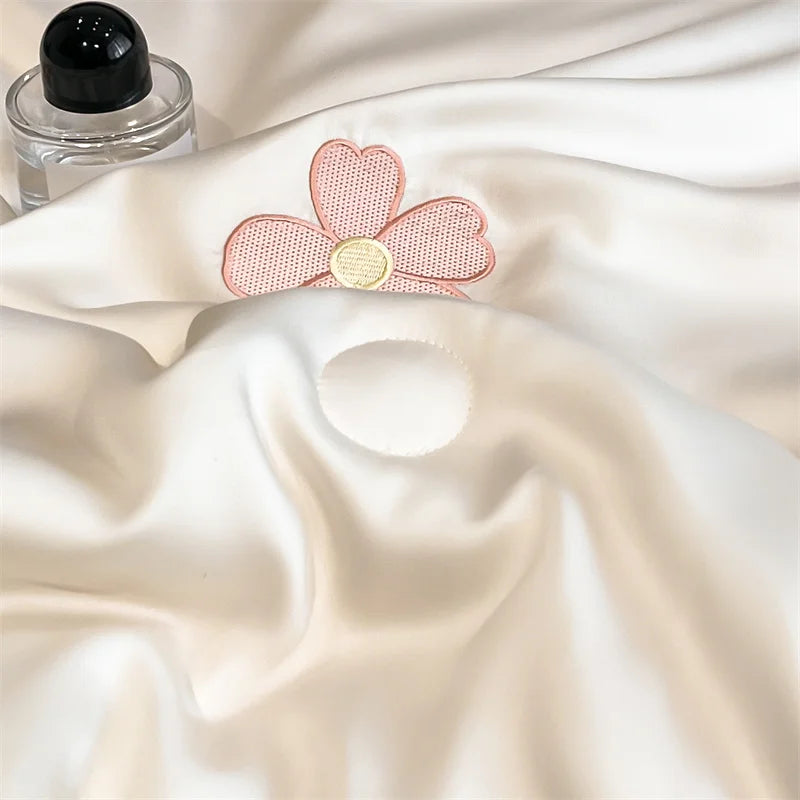 A pink embroidered flower appliqué on a white satin fabric, next to a glass bottle.