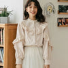 A woman models a cream-colored retro lace long sleeve blouse with ruffled details and a white skirt.