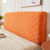 An orange quilted plush headboard cover resting on a light-colored bed.