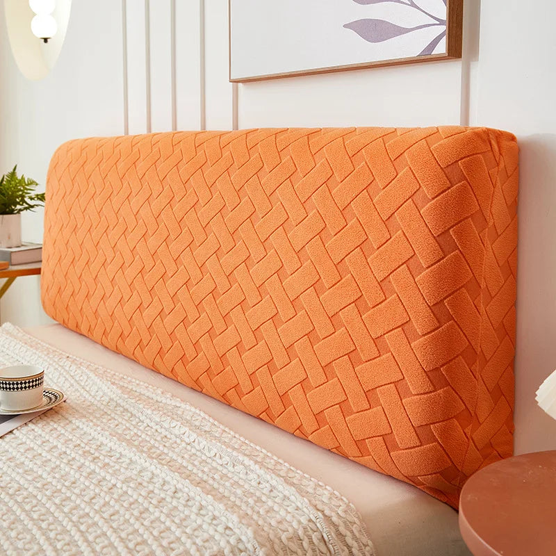 An orange quilted plush headboard cover resting on a light-colored bed.