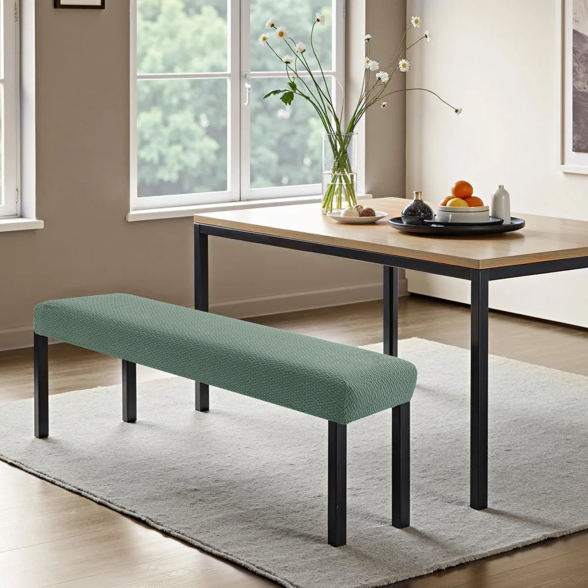 A modern, dark wood dining table is shown with a light green stretch jacquard bench cover and a gray rug in a bright room.