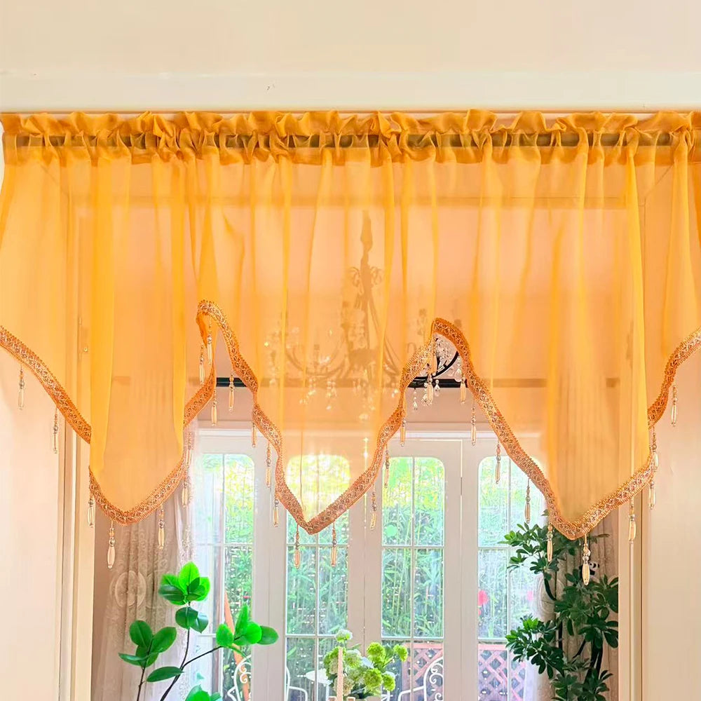 A sheer yellow curtain with heart lace and tassels hangs over a white window frame.