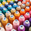 A collection of high tenacity machine embroidery thread spools in various shades of orange, pink, yellow, and blue.