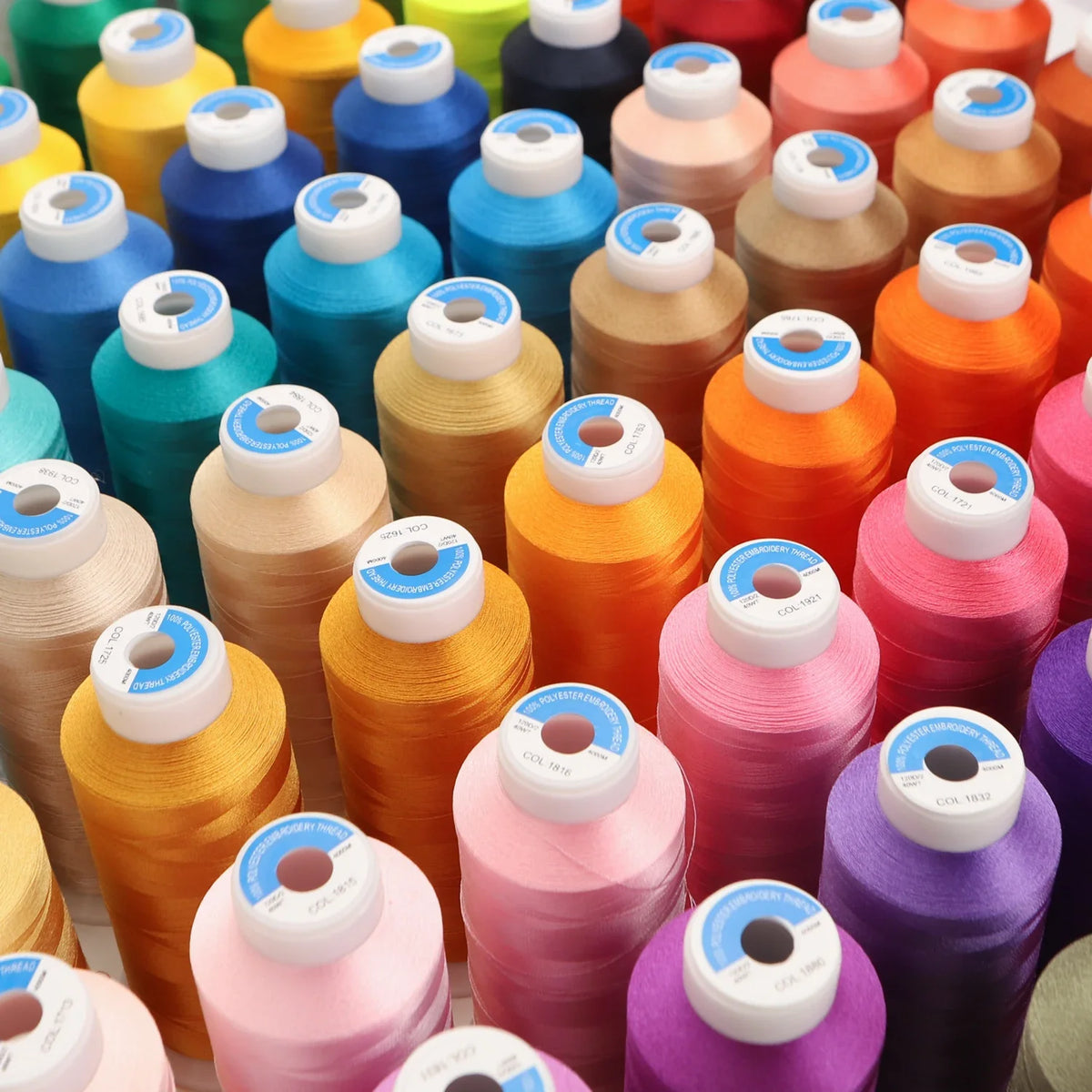A collection of high tenacity machine embroidery thread spools in various shades of orange, pink, yellow, and blue.
