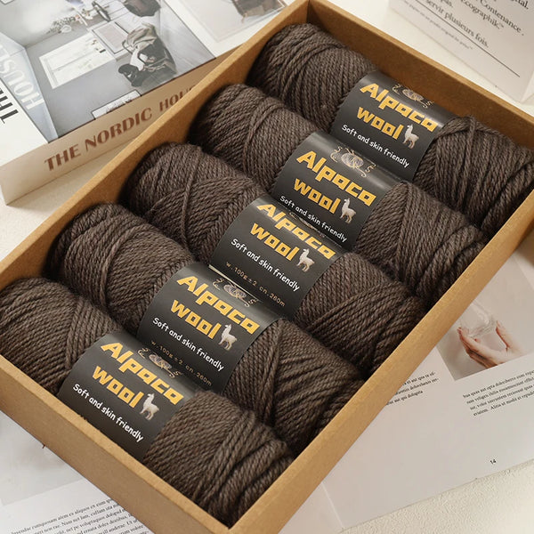 A box of dark brown alpaca wool knitting yarn skeins with labels indicating soft and skin friendly quality.