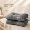 Two gray ergonomic contour pillows are displayed on a white bed with soft lighting.