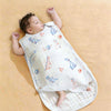 A baby is lying on a quilted white sleeping bag patterned with small birds and animals.