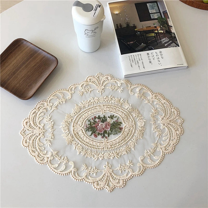 An elegant oval lace embroidered coaster set with a floral design rests on a white surface next to a small white container an