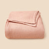 A light pink lightweight cotton waffle blanket folded neatly on a neutral background.