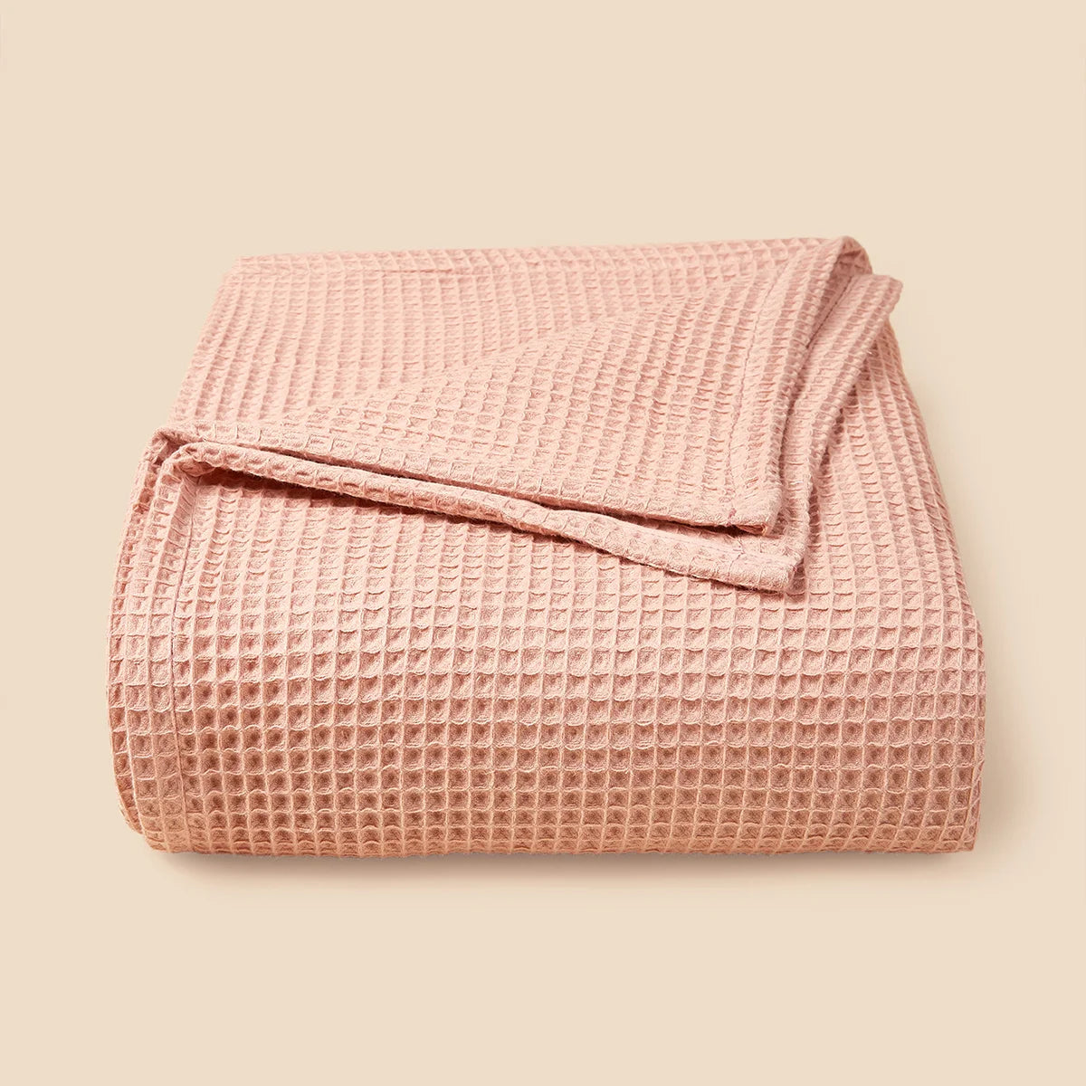 A light pink lightweight cotton waffle blanket folded neatly on a neutral background.