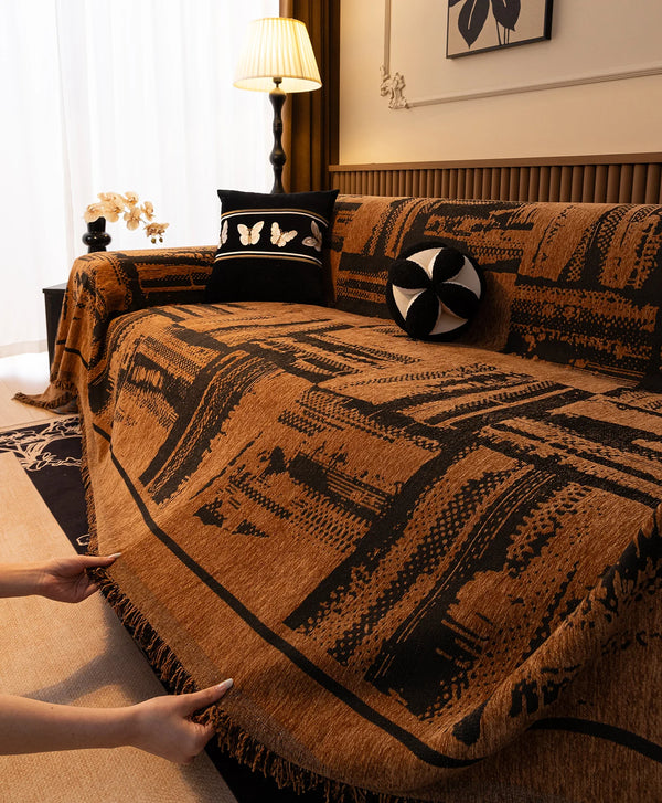 A brown and black vintage patterned sofa throw blanket draped over a sofa in a bright room.