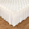 White quilted bed skirt with gold trim draped over a wooden floor.