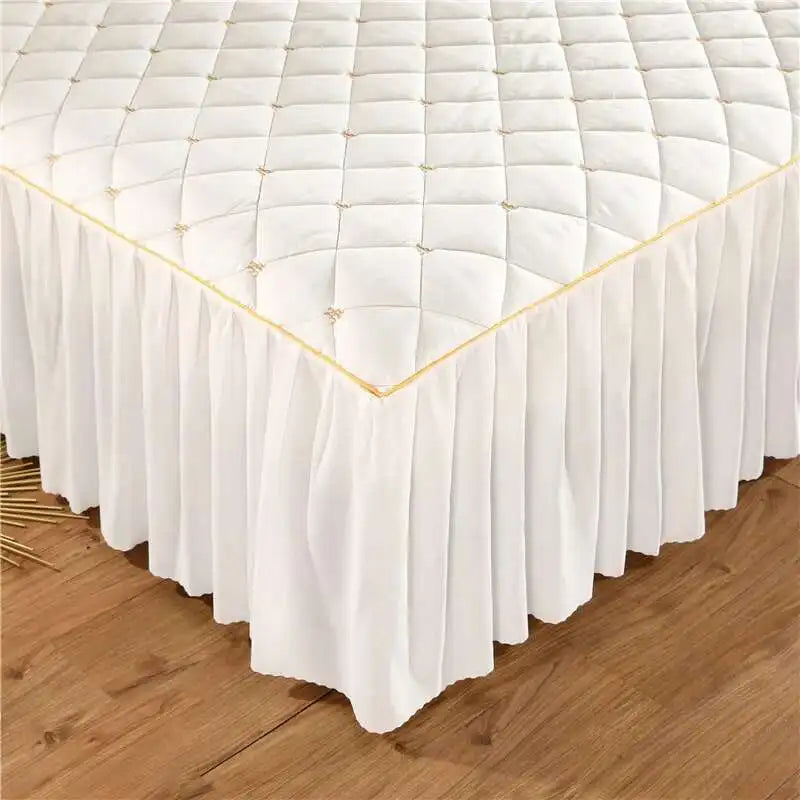 White quilted bed skirt with gold trim draped over a wooden floor.